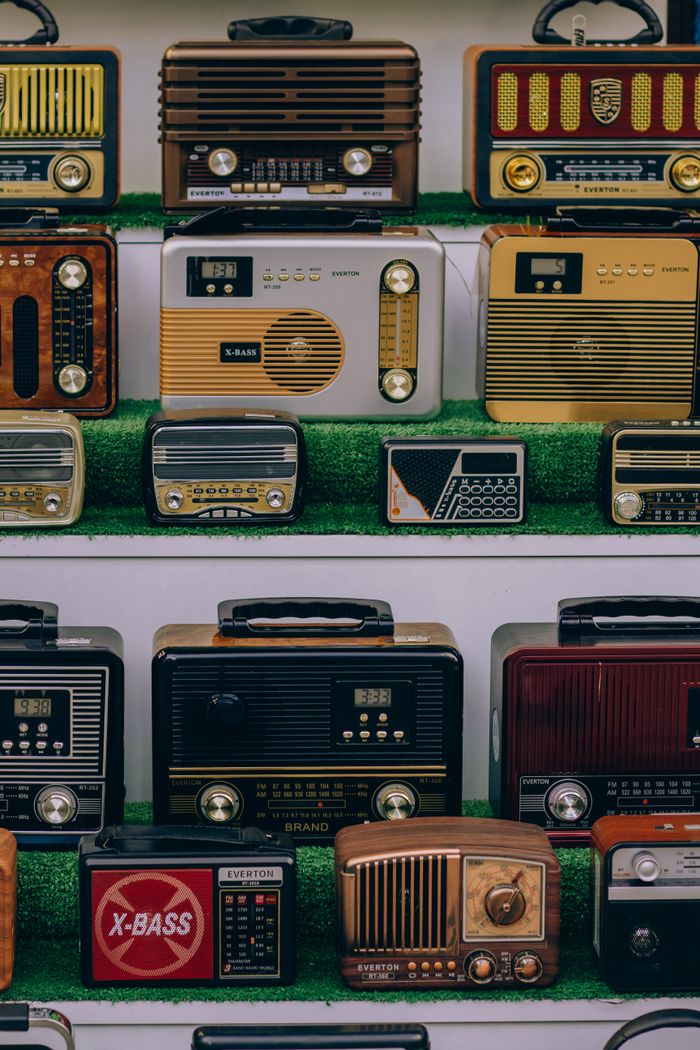 A collection of vintage radios displayed on green-lined shelves. Perfect for retro enthusiasts.